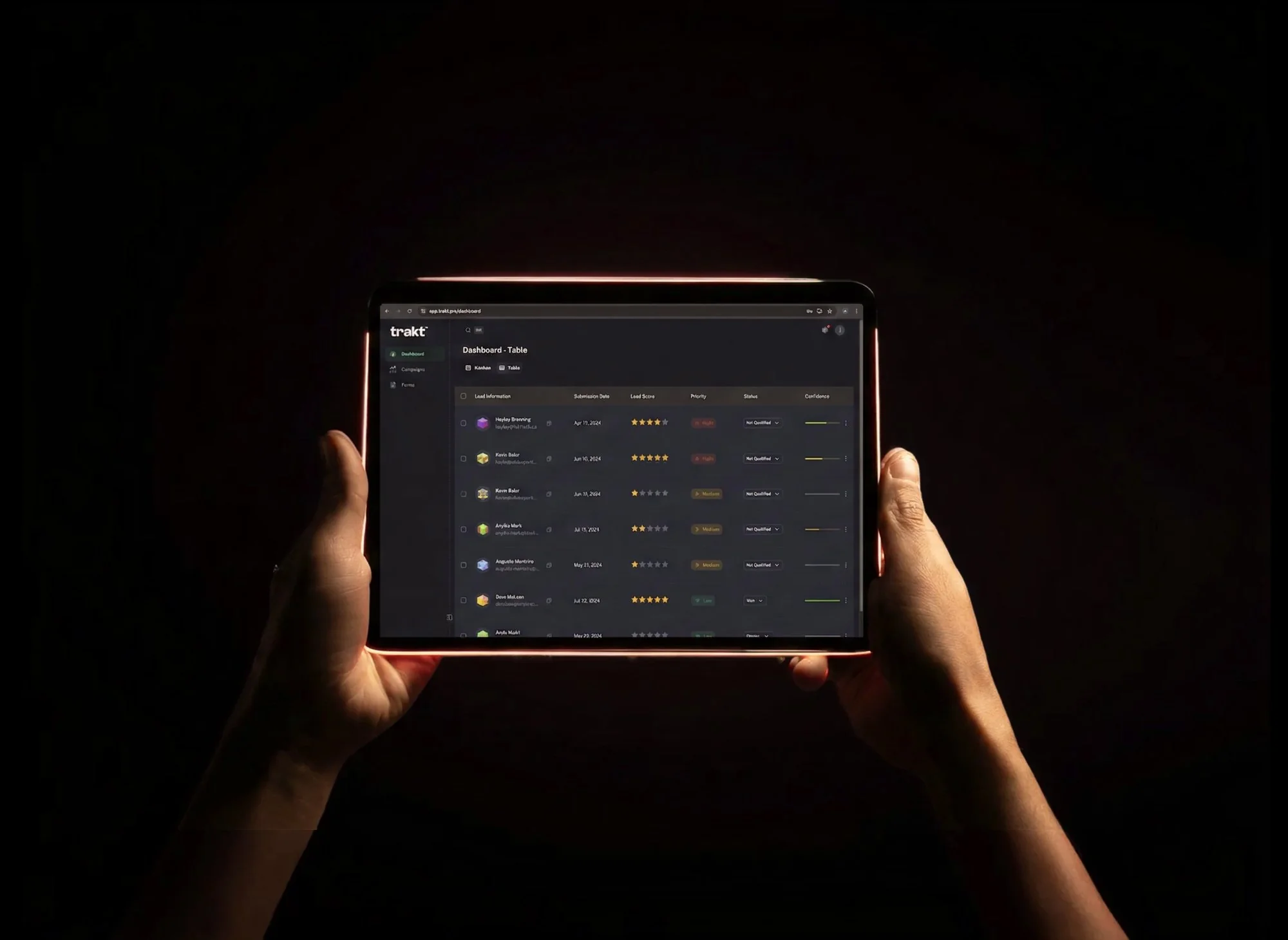 Hands holding a tablet displaying the Trakt dashboard used to track offline tradeshow interactions, with a lead tracking table showing contact information, submission dates, lead scores, priority levels, and status columns against a dark background.