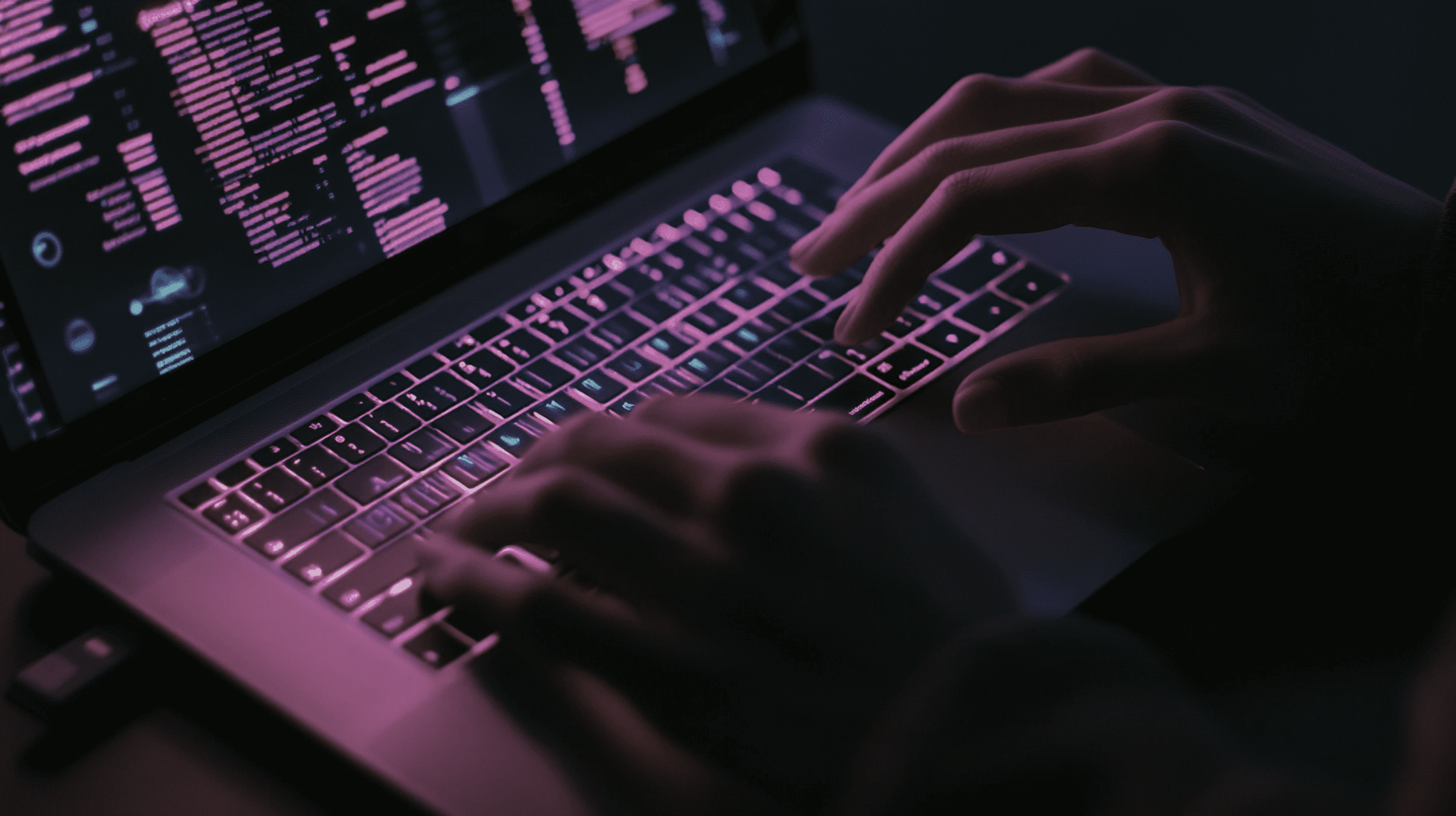 Hands typing on a laptop keyboard with a screen displaying tradeshow lead tracking software, pink and magenta data analytics and code in a dark environment.